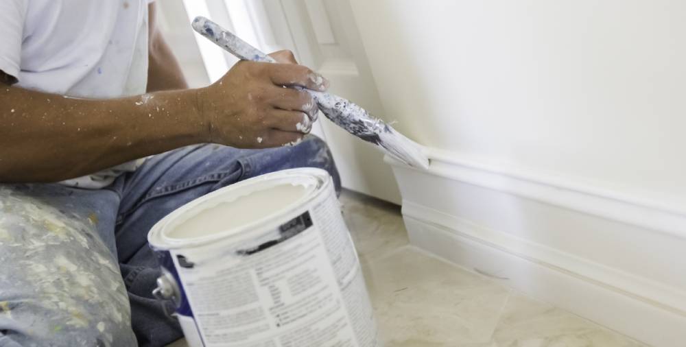 A close up work of a construction interior painter painting a house’s wall wood trim.